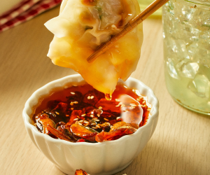 FOOD BEING DIPPED INTO CHILI CRISP SAUCE WITH CHOPSTICKS