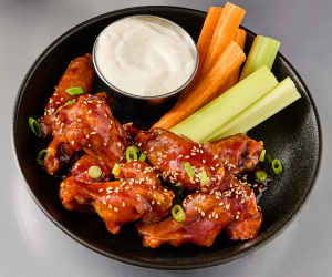 plate of korean bbq wings with celery and carrot sticks