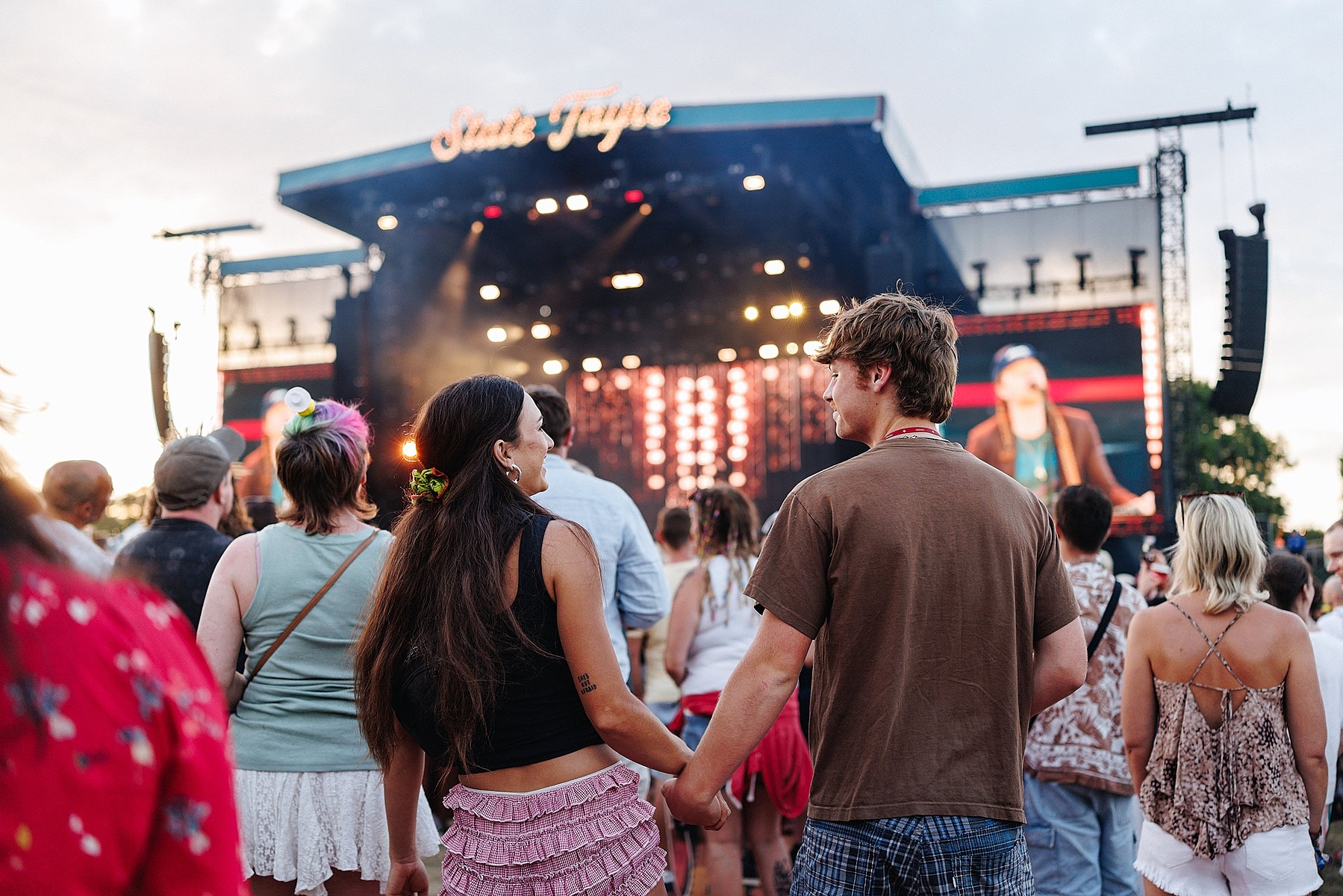 Image of a couple holding hands in front of the State Fayre main stage