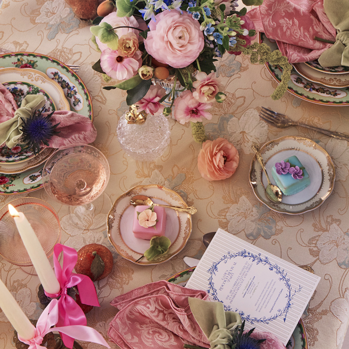Rococo party tablescape with colorful flowers, plates and treats that dot the table. A party invitation designed on Canva sits on one of the plates.
